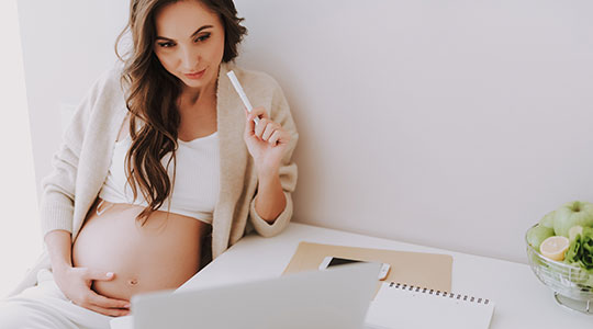 Schwangere Frau mit Stift und Block am Schreibtisch